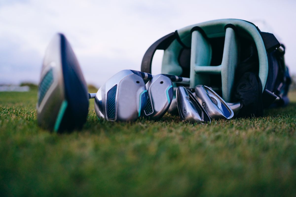 A set of golf clubs lying on the grass beside a golf bag